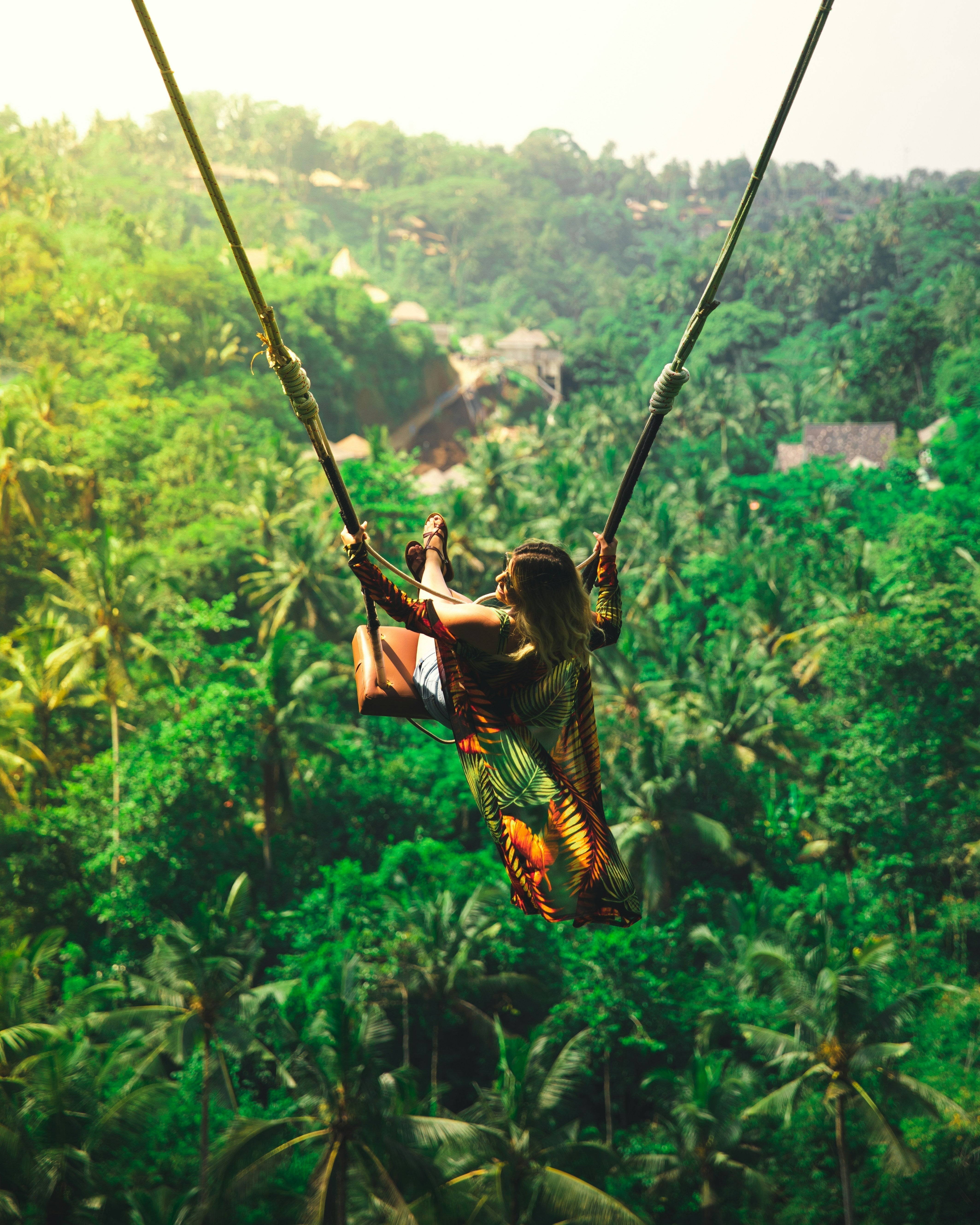 Woman on a swing over lush green Bali forest and trees
